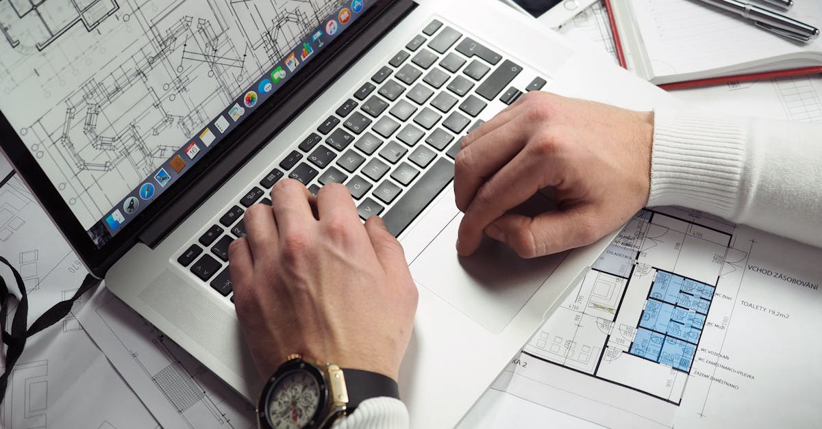 Architect reviewing detailed floor plans and schematics on a laptop with a smartphone nearby.